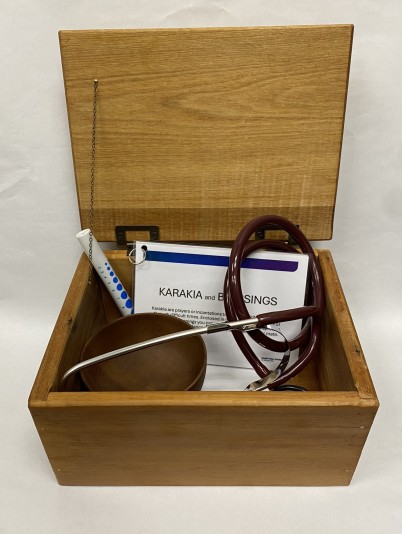 A box containing a stethoscope, pen light, karakia and a wooden bowl.